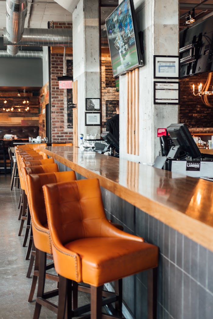 Modern restaurant interior featuring sleek bar stools, exposed brick, and a mounted television.