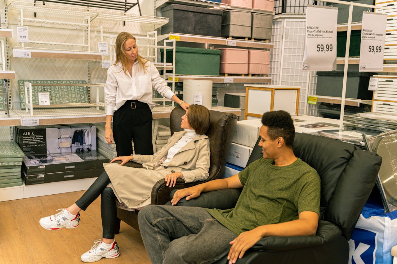 Shoppers try out leather chairs in a modern home furnishings store, guided by a salesperson.